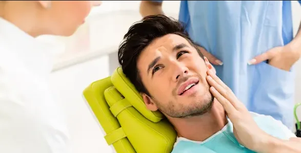 Paziente maschio dal dentista che parla del suo mal di denti. 