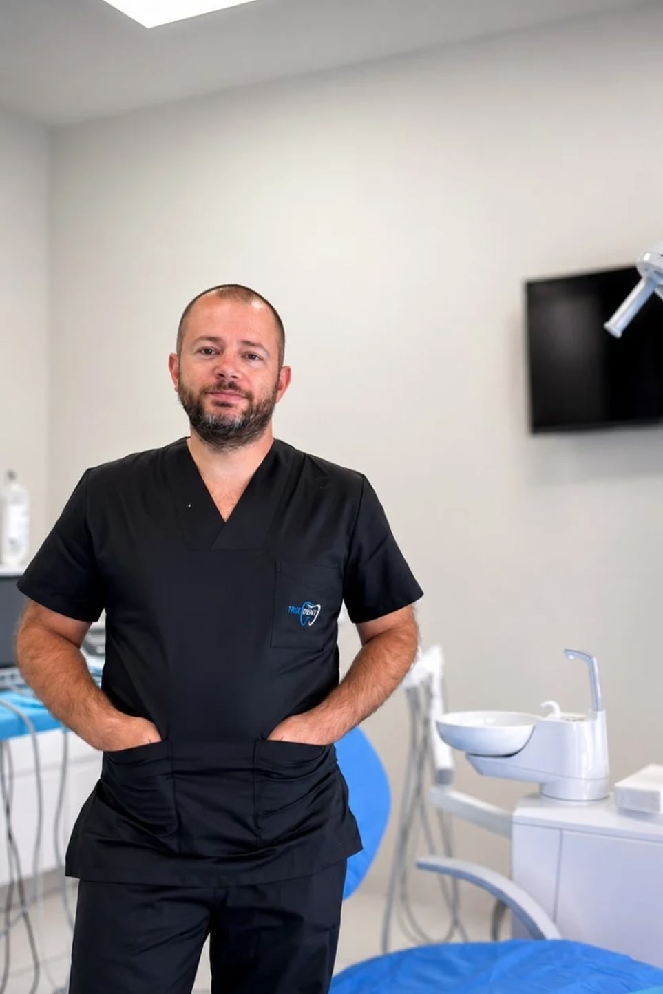Dentist in black scrubs standing in a modern dental office, ready for patient care.