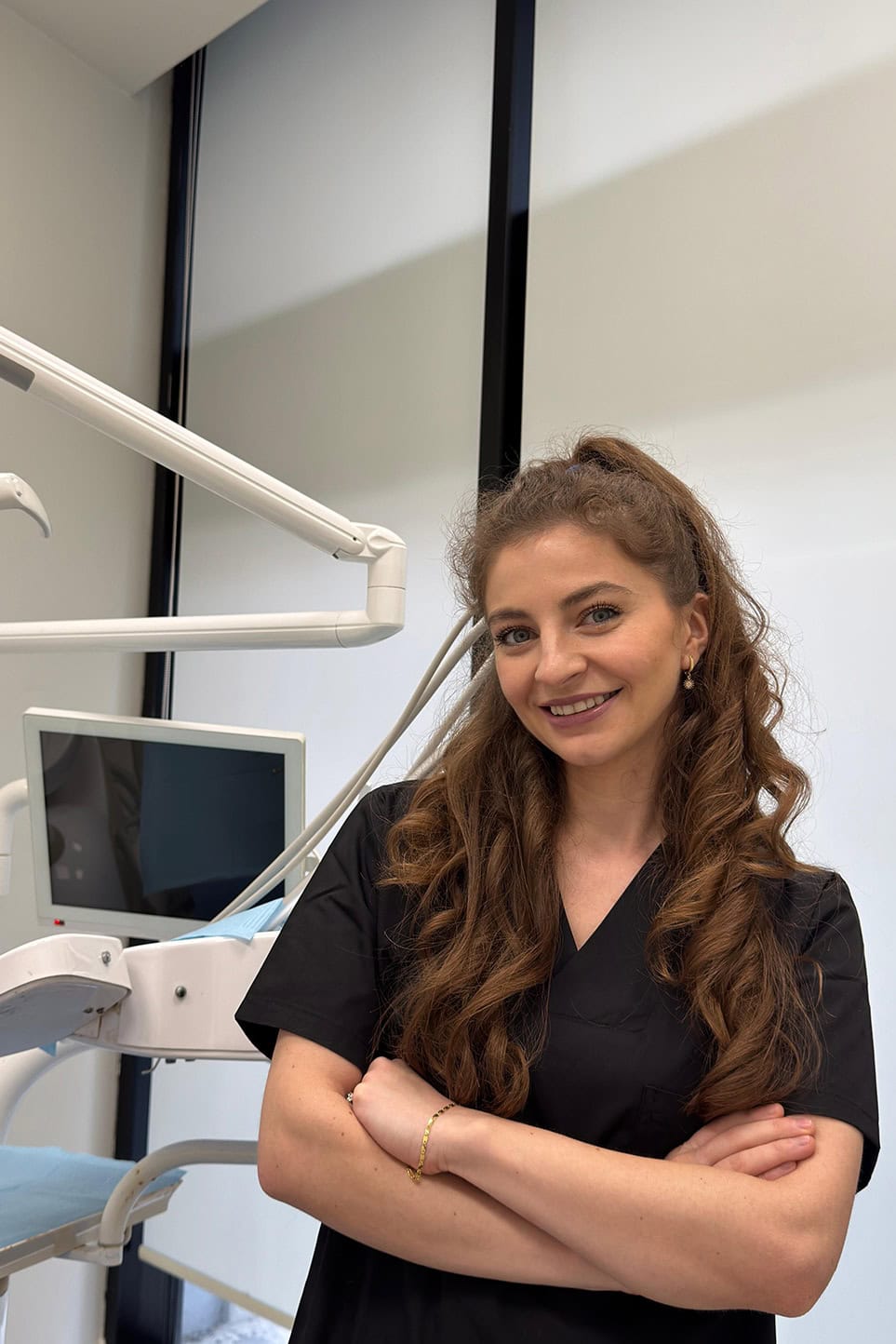 Professionista dentale sorridente in una clinica con le braccia incrociate, attrezzature dentali sullo sfondo.