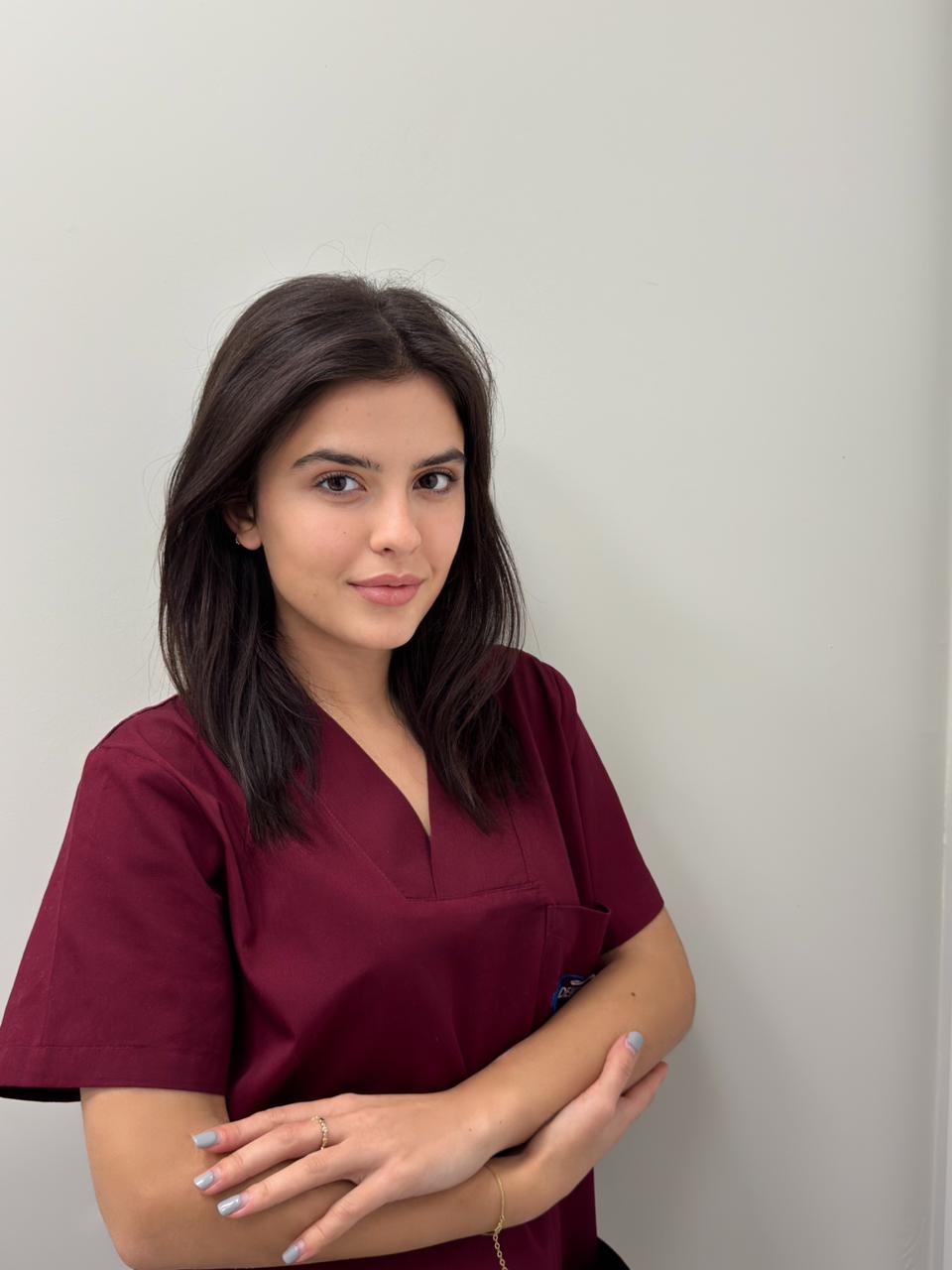 Giovane donna in camice bordeaux, sorridente con le braccia incrociate su sfondo bianco.