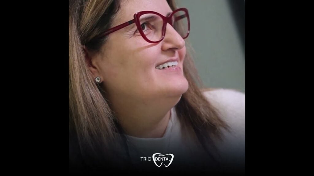 Smiling woman wearing red glasses at Trio Dental clinic, showcasing positive dental care experience.