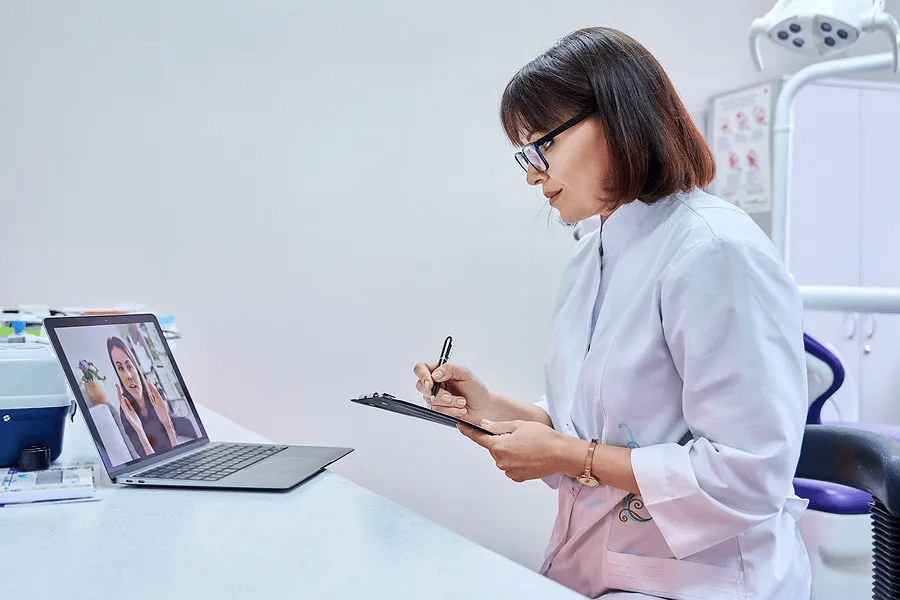 Dentista durante un consulto virtuale, prende appunti durante un incontro online con un paziente in una clinica dentale.