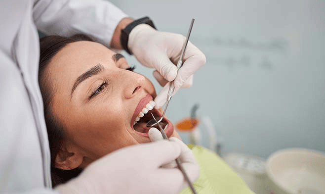 Persona sottoposta a visita odontoiatrica con strumenti nelle mani del dentista, focus sulla bocca aperta e sugli strumenti dentali.