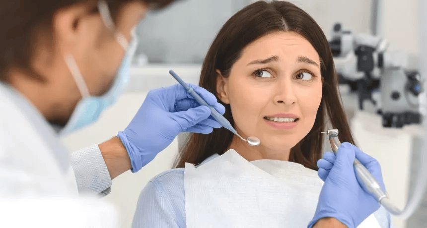 Mujer en la oficina del dentista mirando ansioso durante una revisión dental con el dentista sosteniendo herramientas.