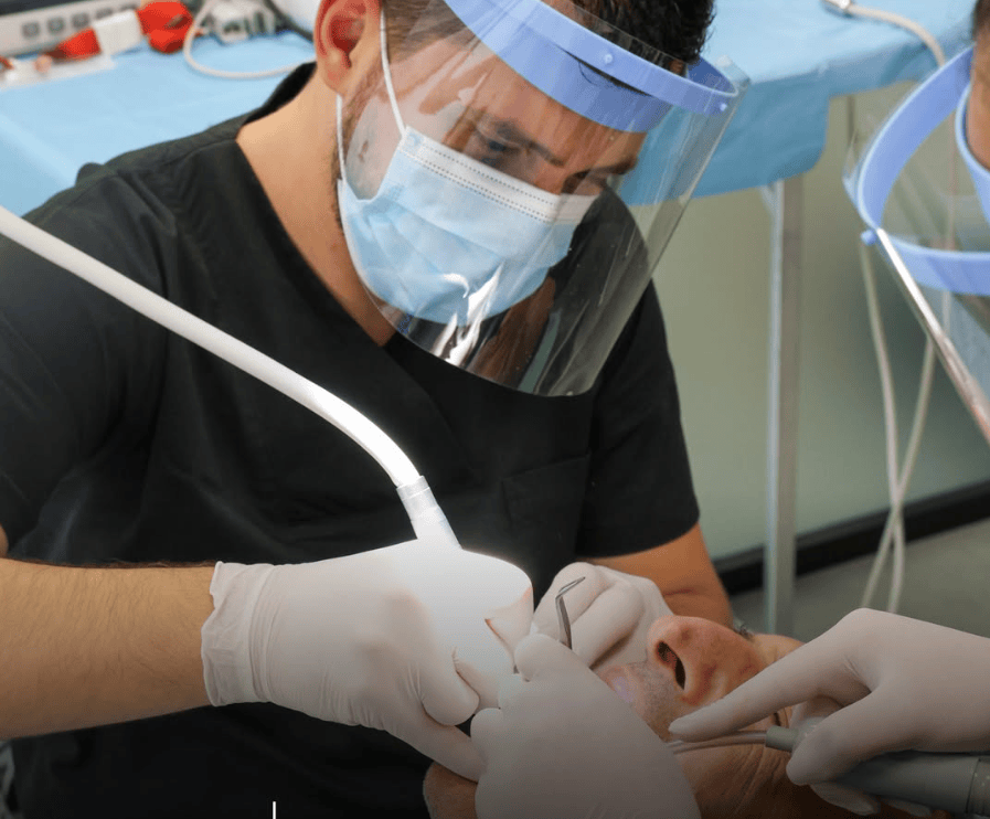 Dentista con visiera e mascherina che esegue una procedura dentale con un assistente in clinica.