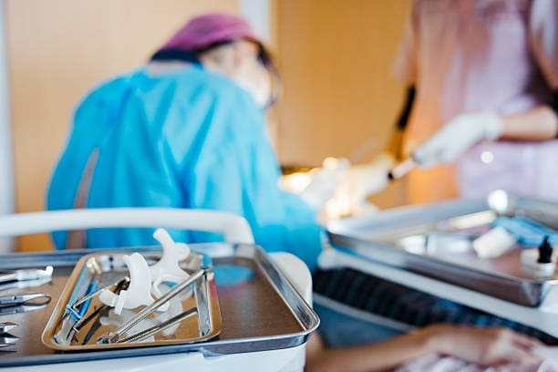 Strumenti dentali su un vassoio con dentisti che eseguono una procedura sullo sfondo.