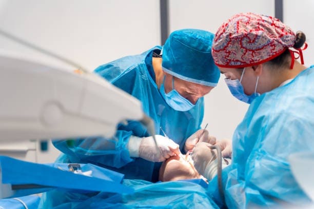 Cirujanos realizando un procedimiento médico en un quirófano, vistiendo batas quirúrgicas azules y mascarillas por seguridad.