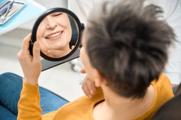 Una persona admira su sonrisa en un espejo en una clínica dental, mostrando cuidado dental y satisfacción con la salud bucal.