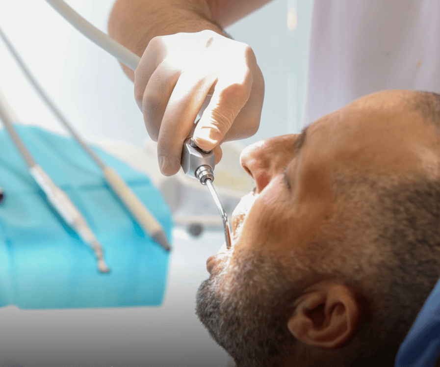 Hombre recibiendo tratamiento dental con herramientas profesionales en un entorno clínico.