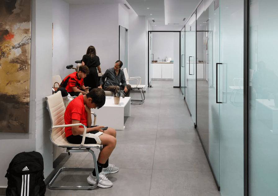 Moderna sala d'attesa con persone sedute, che usano il telefono. Porte in vetro e opere d'arte valorizzano il design contemporaneo dell'ufficio.
