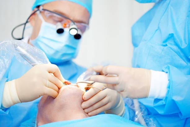 Cirujanos realizando una delicada cirugía ocular con batas y guantes azules en un entorno de quirófano estéril.