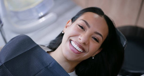 Donna sorridente sulla sedia del dentista, indossa un bavaglino, mostra denti sani e un'esperienza di cura dentale sicura.