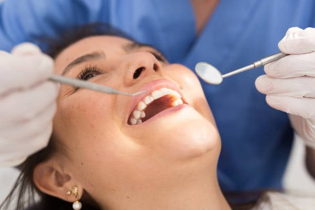 Woman receiving dental check-up, dentist holding mirror and probe, close-up on smiling patient in dental chair.