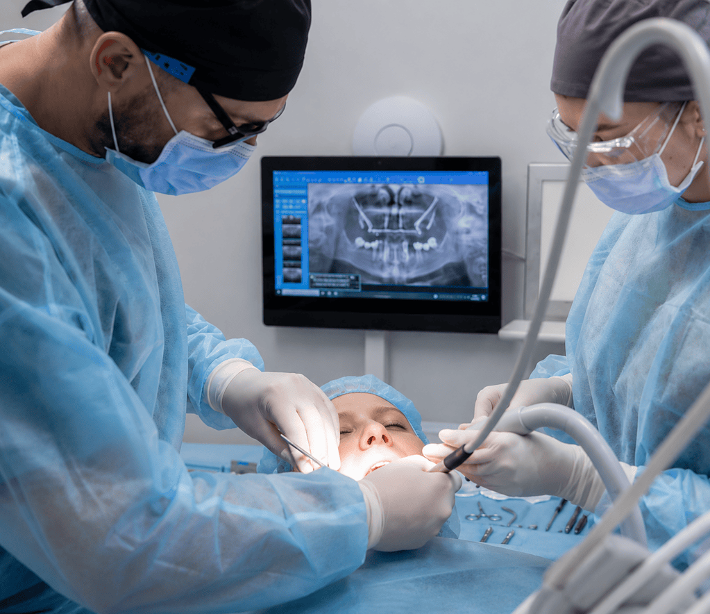 Dentistas realizando cirugía oral con imagen de rayos X en pantalla en una clínica dental moderna.