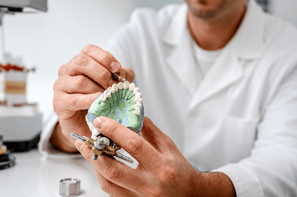 Técnico dental elaborando un modelo dental con herramientas de precisión en un laboratorio.