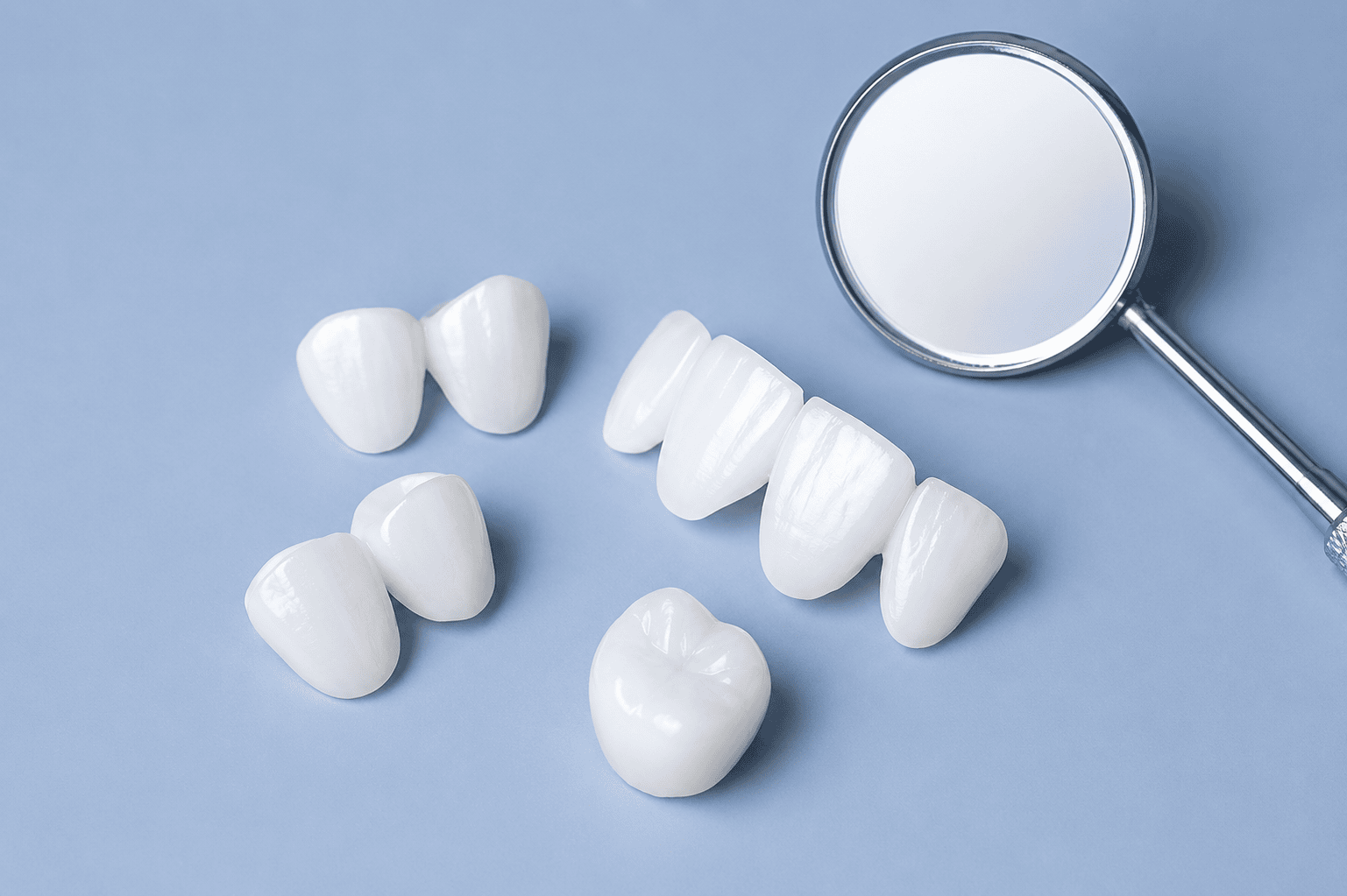 Coronas y carillas dentales con un espejo dental sobre un fondo azul.