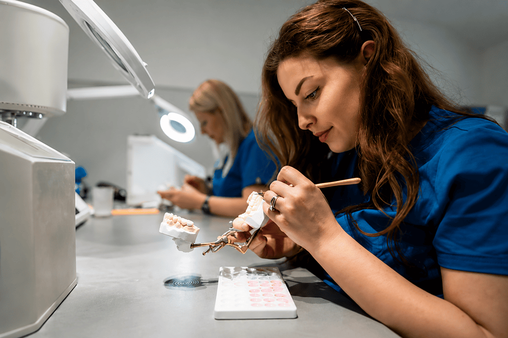 Técnico dental elaborando un modelo de diente en laboratorio con herramientas de precisión.