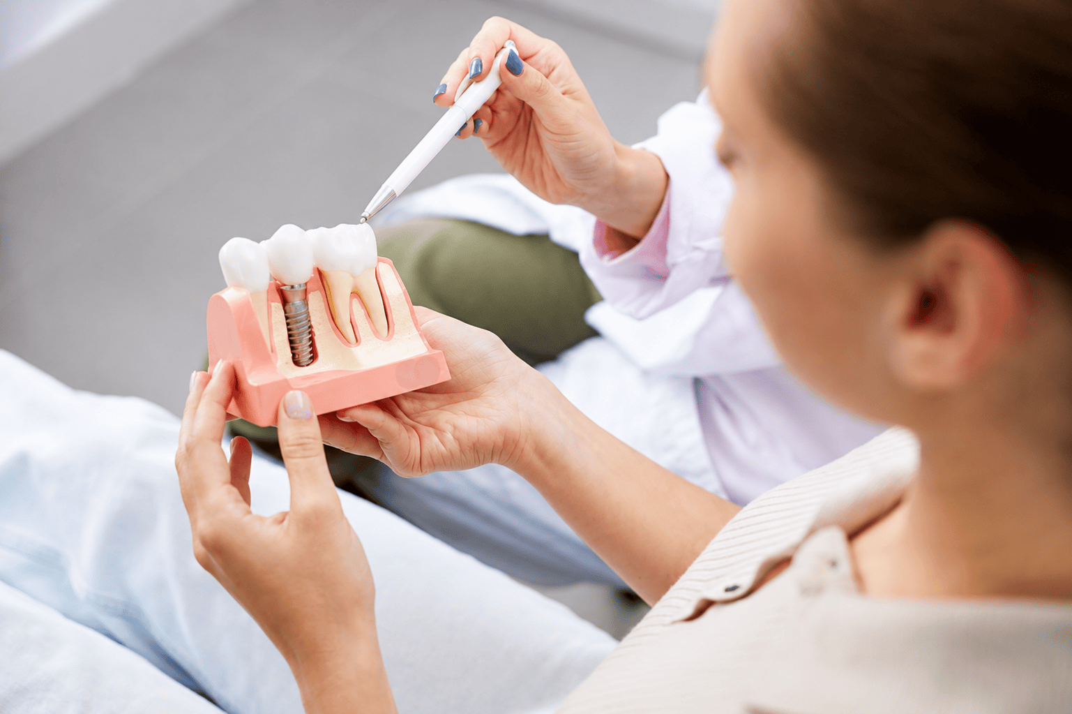 Dentist explaining dental implant model to patient, highlighting tooth structure and procedure details.