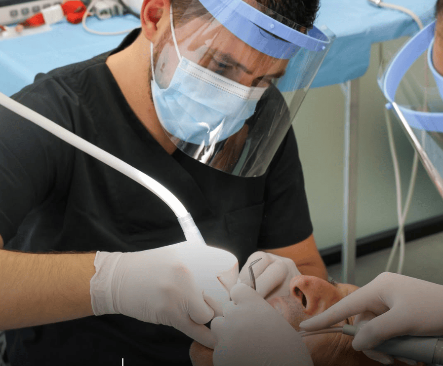 Dentist wearing protective gear performs dental procedure on patient in clinic.