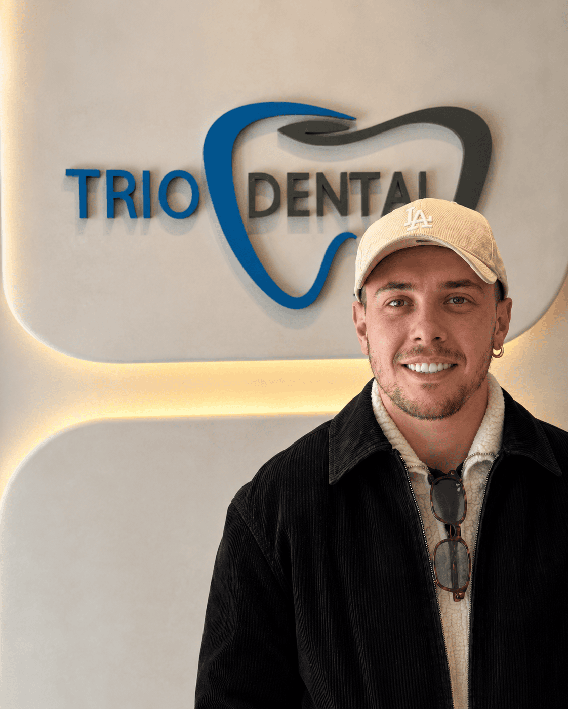 Man smiling in front of Trio Dental logo inside a modern dental office.