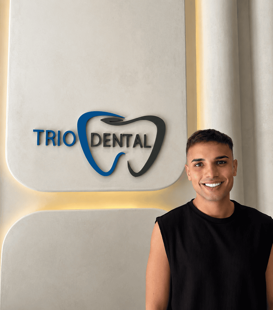 Smiling individual in front of Trio Dental logo on a modern clinic wall.