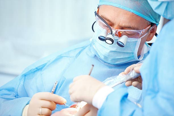 Surgeons performing a precise operation in a sterile environment, wearing surgical masks and magnifying glasses.