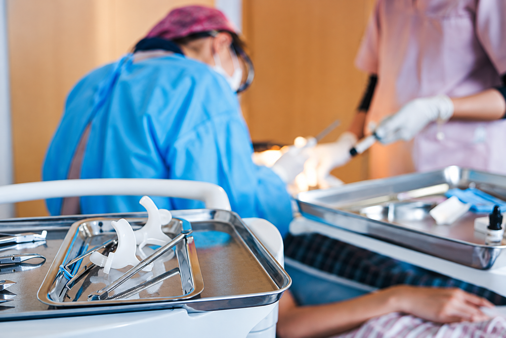 Dentists performing procedure with medical tools on trays in the foreground, highlighting dental care environment.
