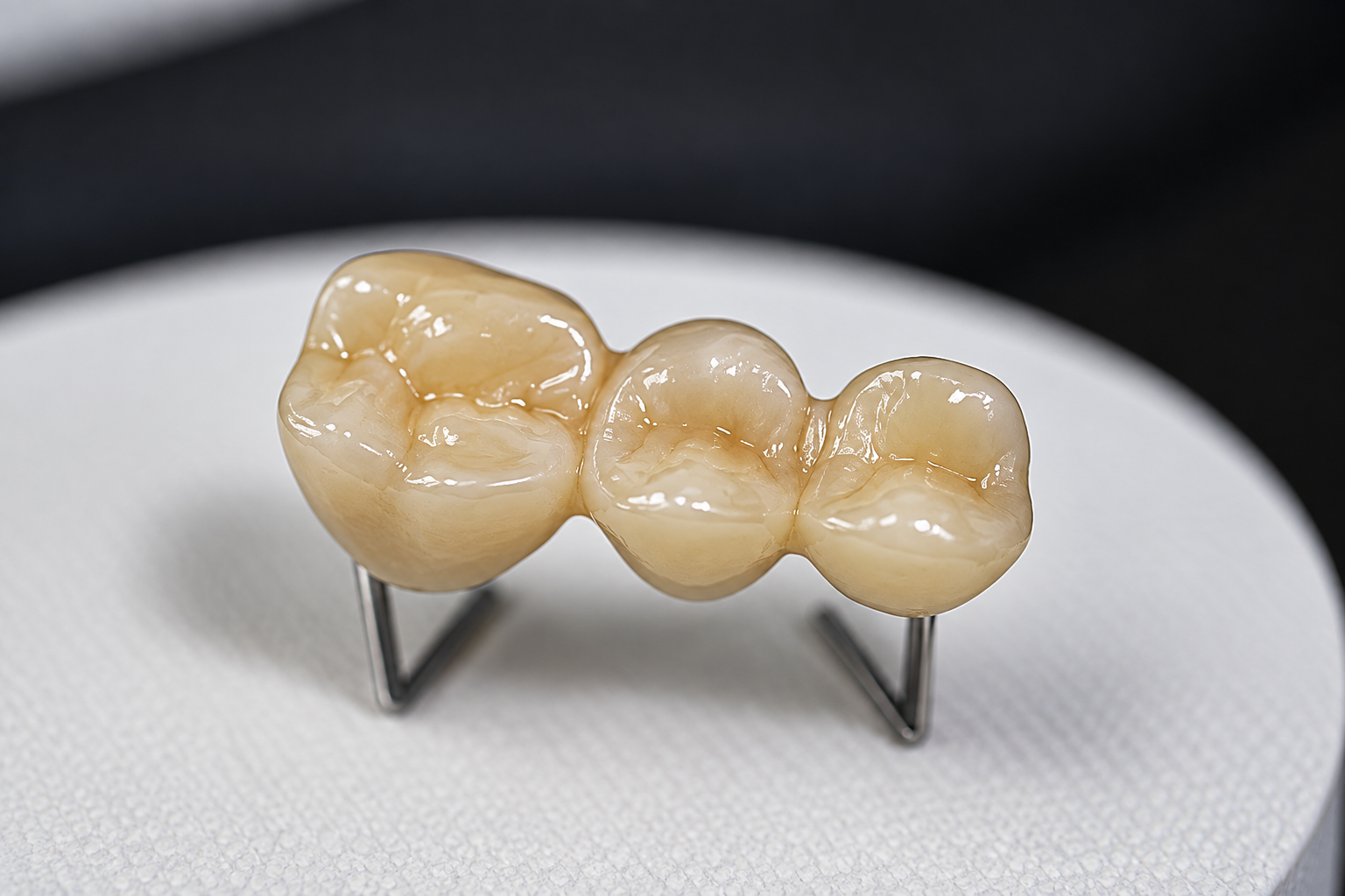 Dental ceramic bridge model displayed on a stand, showcasing realistic tooth structure and shine.